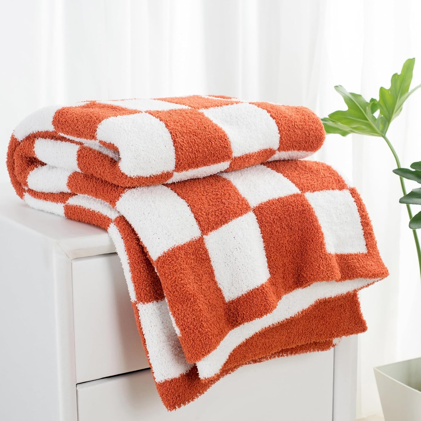 Soft checkered plaid throw blanket in warm tones, gently draped to show its plush, fuzzy texture and knit pattern
