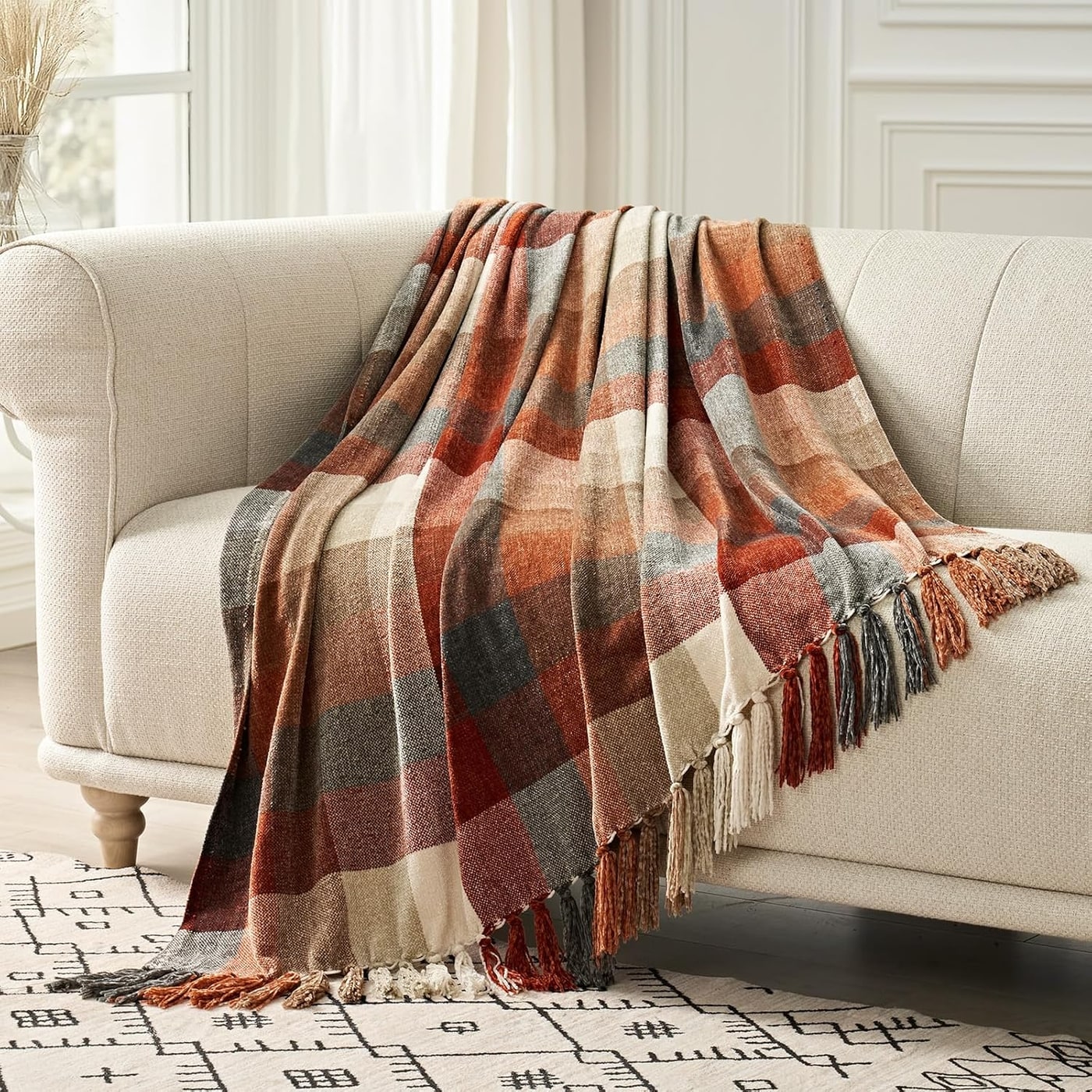 Chenille plaid knit throw blanket with tassels displayed draped over a sofa, showing soft texture and a classic plaid design.