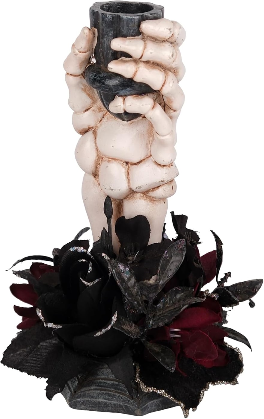 Bone-white resin skeleton hand candlestick with black faux flower holding a taper candle, displayed on a tabletop.
